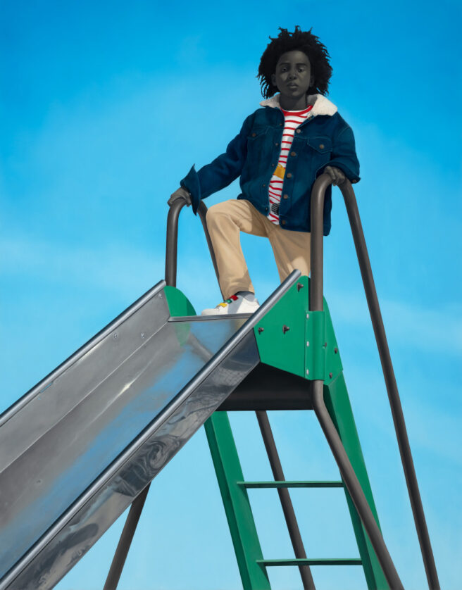 A young person with gray-toned skin and dark, curly hair stands on top of a playground slide, wearing a denim jacket, a striped shirt, and tan pants. The slide has a green frame and a silver surface, set against a clear blue sky.
