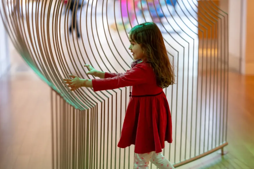 A little girl smiles while she feels a wire sculpture of Mary Flanagan’s Topophilia (Tunnel) and Topophilia (Hill) inside the Joseph Education Center at the Baltimore Museum of Art